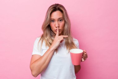 Pembe kupa tutan genç Avustralyalı kadın pembe arka planda izole edilmiş bir şekilde bir sır saklıyor ya da sessizlik istiyor..