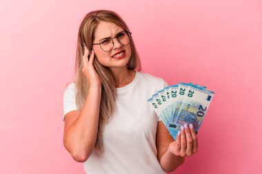Elinde banknotlar tutan genç Rus kadın pembe arka planda izole edilmiş kulakları elleriyle kapatıyor..