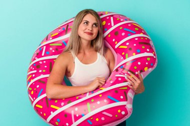 Şişme donutlu genç Rus kadın mavi arka planda izole edilmiş hedeflerine ve amaçlarına ulaşma hayali kuruyor.