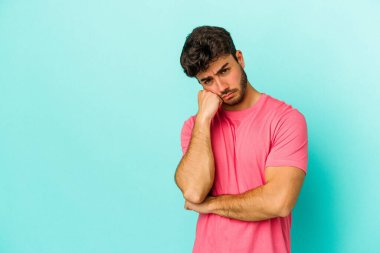 Mavi arka planda izole edilmiş, üzgün ve dalgın hisseden, kopyalama alanına bakan genç beyaz bir adam..