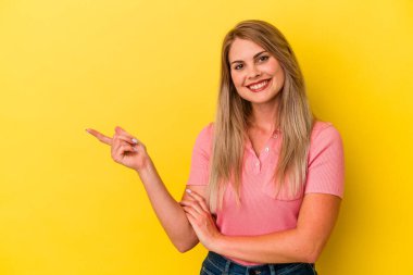 Sarı arka planda izole edilmiş genç Rus kadın işaret parmağıyla işaret ederek gülümsüyor..