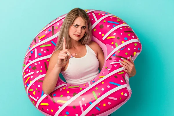 Şişme donutlu genç bir Rus kadın mavi arka planda izole edilmiş ve parmağıyla bir numarayı gösteriyor..