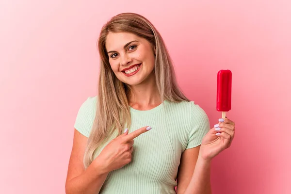 ピンクの背景に孤立したアイスクリームを持っている若いロシアの女性は笑顔と脇を指して 空白のスペースで何かを示しています — ストック写真