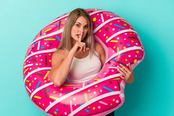 Şişme donutlu genç Rus kadın mavi arka planda izole edilmiş ya sır saklıyor ya da sessizlik istiyor..