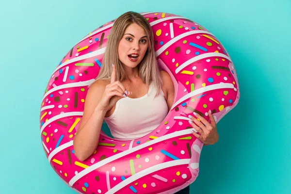 Şişme donutu olan genç Rus kadın mavi arka planda izole edilmiş. Harika bir fikri var, yaratıcılık kavramı..