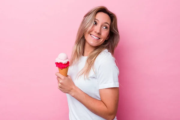 拿着一个粉色背景的冰淇淋的年轻的澳大利亚女人 面带微笑 快乐而愉快 — 图库照片