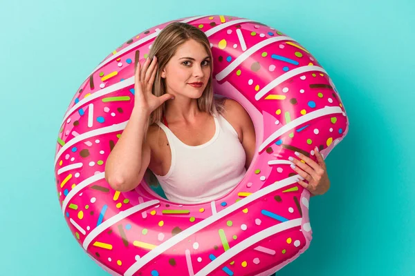 Şişme donutlu genç bir Rus kadın mavi arka planda izole edilmiş bir şekilde bir dedikoduyu dinlemeye çalışıyor..