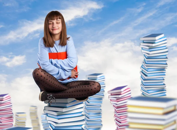 Ung kvinna sitter på böcker tower — Stockfoto