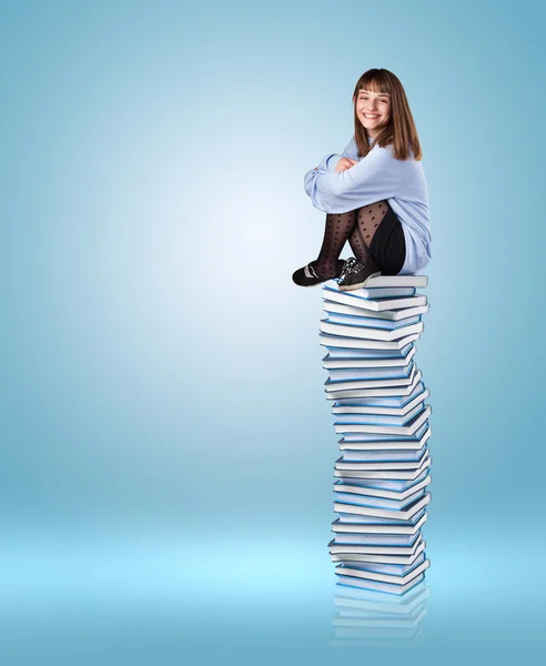 Ung kvinna sitter på böcker tower — Stockfoto