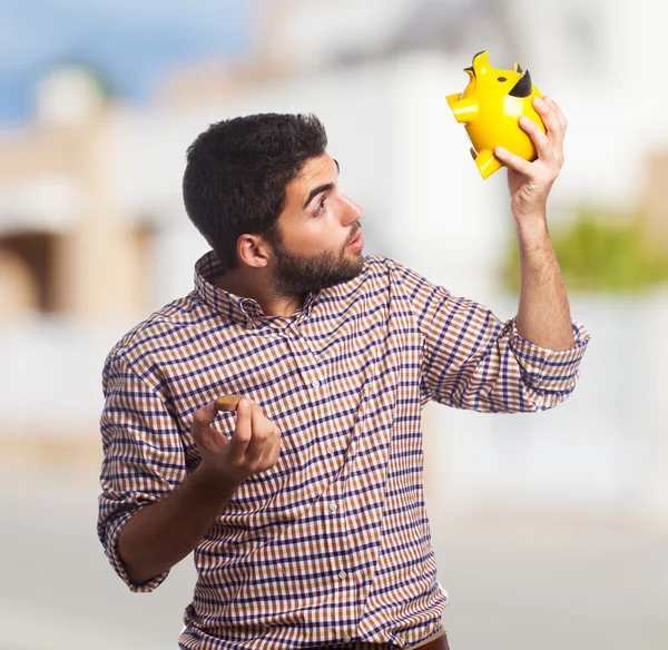 Schöner Mann schaut ins Sparschwein — Stockfoto