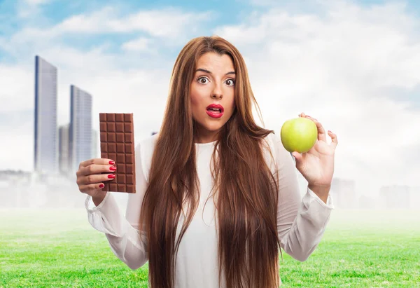 Девушка выбирает между шоколадом и яблоком — стоковое фото