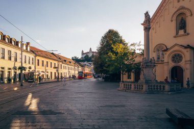 Bratislava cazibesini güneş ışığıyla, sokaklara düşen gölgelerle, yürüyen insanlarla ve yukarıdaki şatoyla birlikte tarihi binalarla sergiliyor..