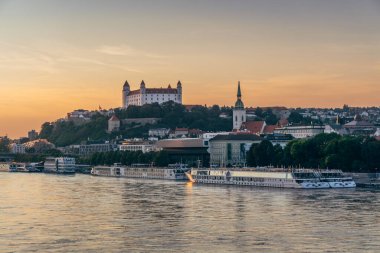 Günbatımı, Bratislava 'nın eski kasabasına altın ışık tutuyor. Tepedeki şatoyu ve Tuna Nehri' ndeki tekneleri aydınlatıyor..