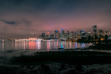 Ufuk çizgisi modern binaları gösterirken parlak şehir ışıkları sakin suları yansıtıyor. Sahne, açık bir gecede rıhtımın huzurlu havasını yakalıyor..
