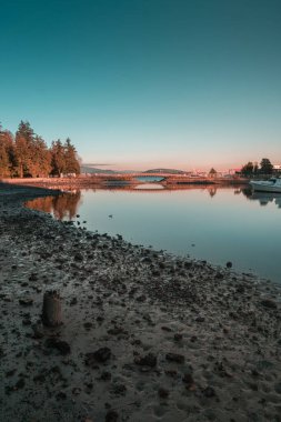 Tranquil scene shows calm water reflecting the evening sky with trees lining the shore at sunset, creating a peaceful atmosphere.