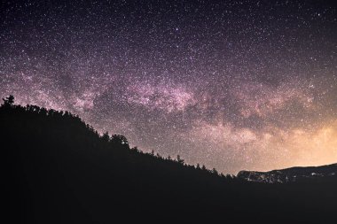Stars twinkle brightly in the night sky above a silhouetted mountain range, creating a breathtaking view of the universe.