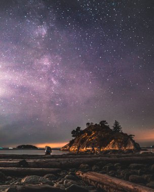 A serene beach scene showcases a clear night sky filled with stars. A small island stands out under the cosmic display, creating a stunning view.