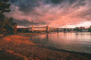 Nehrin üzerinde güzel bir günbatımı dramatik bulutlar ve bir köprü sergiliyor. Suyun kenarında sakin bir atmosfer yaratıyor..