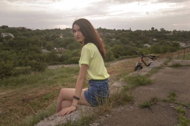 Genç bir kız kaldırımda oturur ve yaz şehrine bakar. Manzara yüksek bir açıdan açılır. Kız geçenlerde bisiklete bindi - ondan uzak değil. Kameraya bakan bir kızın düşünceli görüntüsü..