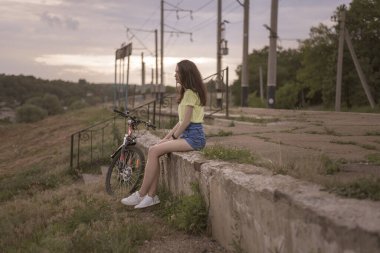 Eski bir istasyonun platformunda tek başına oturan ve şehri izleyen bir kız resmi. Küçük bir kasabaya tepeden bakan yüksek bir yerden, kızın bisikletinin yanına..