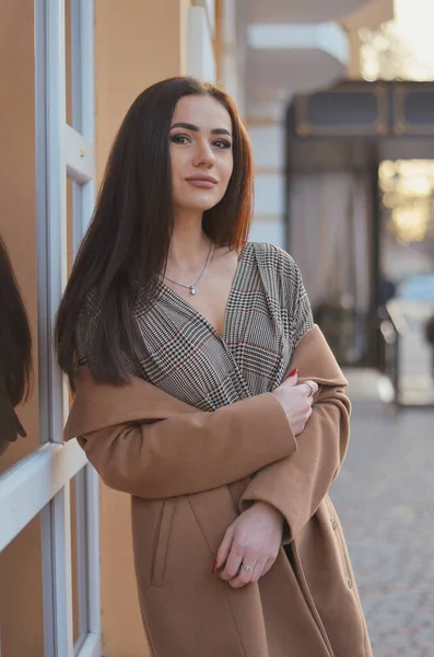Palto ve bluz giymiş bir kız duvarın yanında duruyor.. 