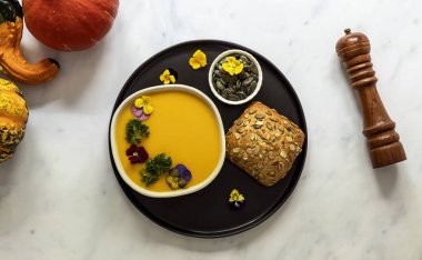 Yenebilir çiçekler, tohum ve taze pişmiş ekmekle sonbahar balkabağı kreması çorbası..