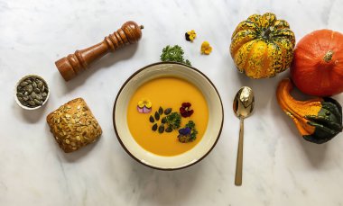 Yenilebilir çiçekler, tohumlar ve taze pişmiş ekmekle balkabağı kremalı çorba. Sağlıklı vejetaryen güz yemeği.