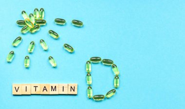 Yuvarlak kasede sarı kapsüller ve mavi arka planda tahta küplerin D vitamini. Kopyalama alanı ile sağlıklı konsept. 
