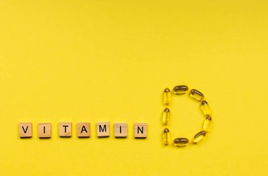 D harfi şeklinde sarı kapsüller ve içinde vitamin, sağlıklı ve tıbbi konsept harfleri olan tahta küpler. Boşluğu kopyala
