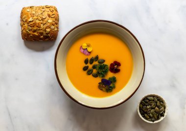 Vejetaryen sonbahar balkabağı kremalı çorba, yenilebilir çiçekler, tohum ve taze pişmiş ekmek..