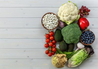 Sağlıklı gıda arka planı, modaya uygun bitki temelli diyet ürünleri - taze çiğ sebzeler, meyveler ve fasulyeler. Doğal ahşap masa, boşluğu kopyala