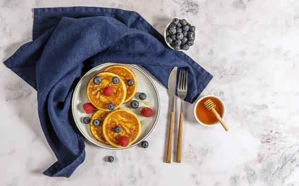 Ein Teller mit leckeren amerikanischen Pfannkuchen mit Himbeeren, Blaubeeren und Honig. Draufsicht, Marmortisch. — Stockfoto