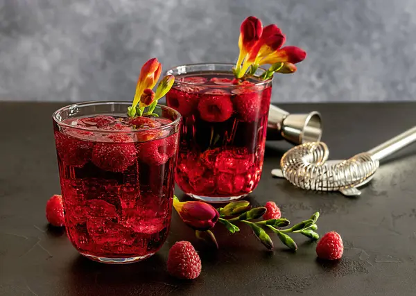 Fresh berries cocktail with gin, raspberry, soda water, and ice in glass on dark background. Summer cold alcohol drink.