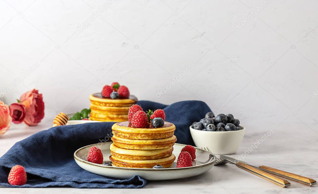 Two plates with american pancakes with raspberries, blueberries, and honey. 