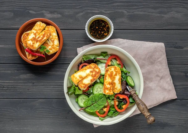 Kızarmış Halloumi peynirli salata, salatalık, kırmızı biber, yeşil soğan ve yapraklı. Sağlıklı gıda konsepti, üst manzara, ahşap masa.