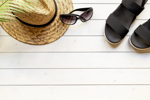 Women\'s open-toe black sandals from recycled plastic fibers, straw hat, sunglasses on the wooden boardwalk. Summer traveling concept.