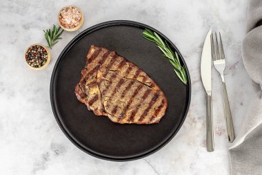 Geleneksel entrecote, kaburgadan kesilmiş. Tabakta orta boy kaburga bifteği, çatal bıçak takımı ve baharatlarla. Yukarıya bak.