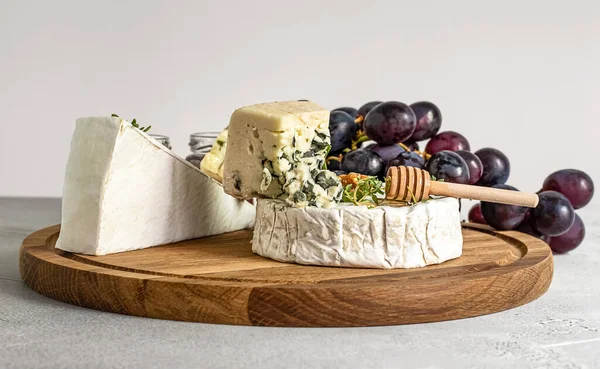 Camembert, Roquefort en brie kaas met honing, druiven en walnoten op de snijplank. — Stockfoto