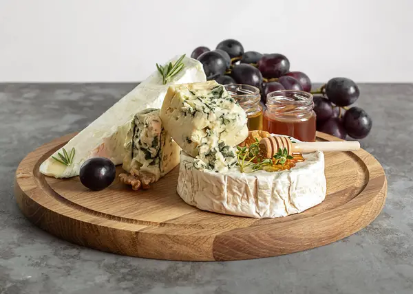 Camembert, Roquefort en brie kaas met honing, druiven en walnoten op de snijplank. — Stockfoto