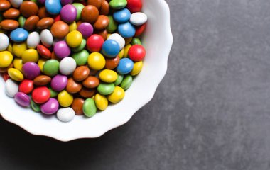 Birçok renkli tatlı gri bir arka planda beyaz bir tabakta uzanır. Boşluğu kopyala