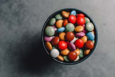 Birçok renkli tatlı gri bir arka planda siyah bir tabakta uzanır. Boşluğu kopyala