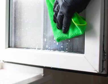 Kirli camları siliyorum. Siyah eldivenli, sprey deterjanlı bir kadın. Ev temizliği, temizlik hizmetleri.