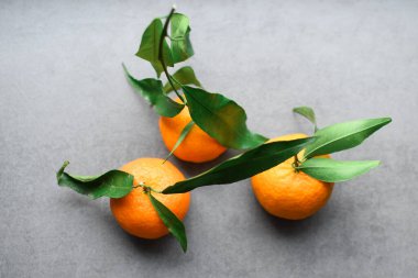Gri arka planda yeşil yapraklı taze turuncu mandalina. Yiyecek uçurma konsepti. Sağlıklı yiyecekler, olgun meyveler, turunçgiller..