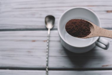 Tahta kaşık, beyaz bir fincanın üzerinde, retro kaşığın yanında duran, öğütülmüş kahveyle dolu. Yukarıdan görüntüle.