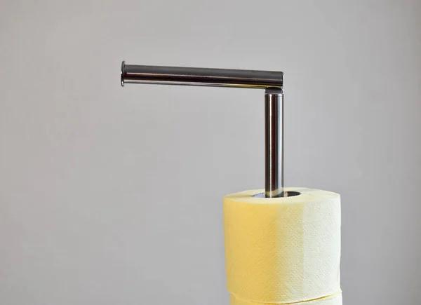 Floor-standing metal holder for toilet paper. Yellow rolls of paper on a gray background. Isolated