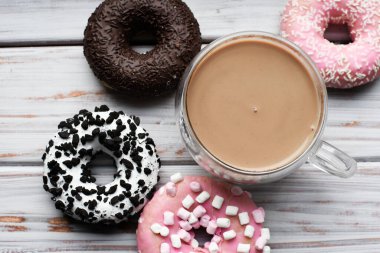 Tatlı ve renkli çörekler, ahşap arka planda bir fincan kapuçino ile yakın plan..