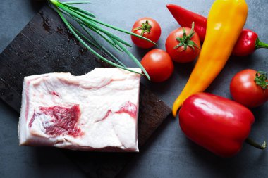 Çiğ domuz yağıyla ahşap bir tahta üzerinde et ve fotokopi alanı için gri arka planda sebzeler. Büyük bir parça taze yağ. Ukrayna domuzu, geleneksel yiyecekler.