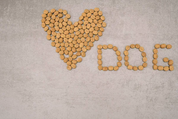 Dry dog food, lined with hearts with the inscription dog on a gray background. Healthy balanced dog food. Pet care