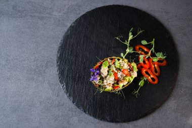 Avokado atıştırmalıkları, renkli, lezzetli, siyah bir tabakta yatıyor. Kıyma, avodako, dolma biber, dereotlu mikroçerez, soğan ve menekşe çiçekle süslenmiş..