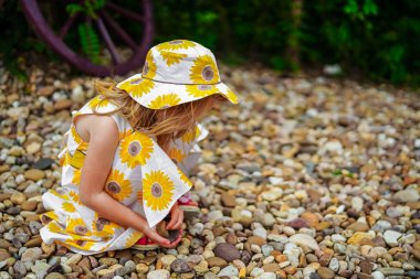 Sevimli 4 yaşında sarışın bir kız bahçede yürüyor, oynuyor ve yaz ayçiçeği elbisesi giyiyor.